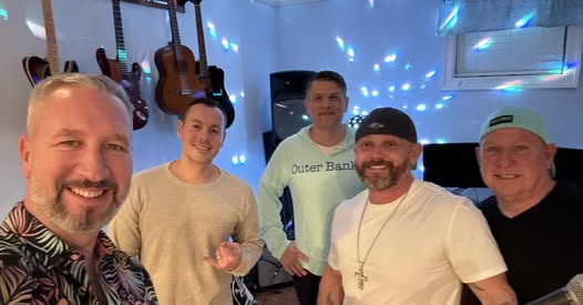 Group of five men enjoying music at Port of Leonardtown Winery with guitars on the wall.