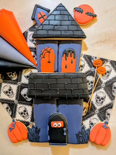 Halloween-themed haunted house cookie with orange, black, and blue icing details.